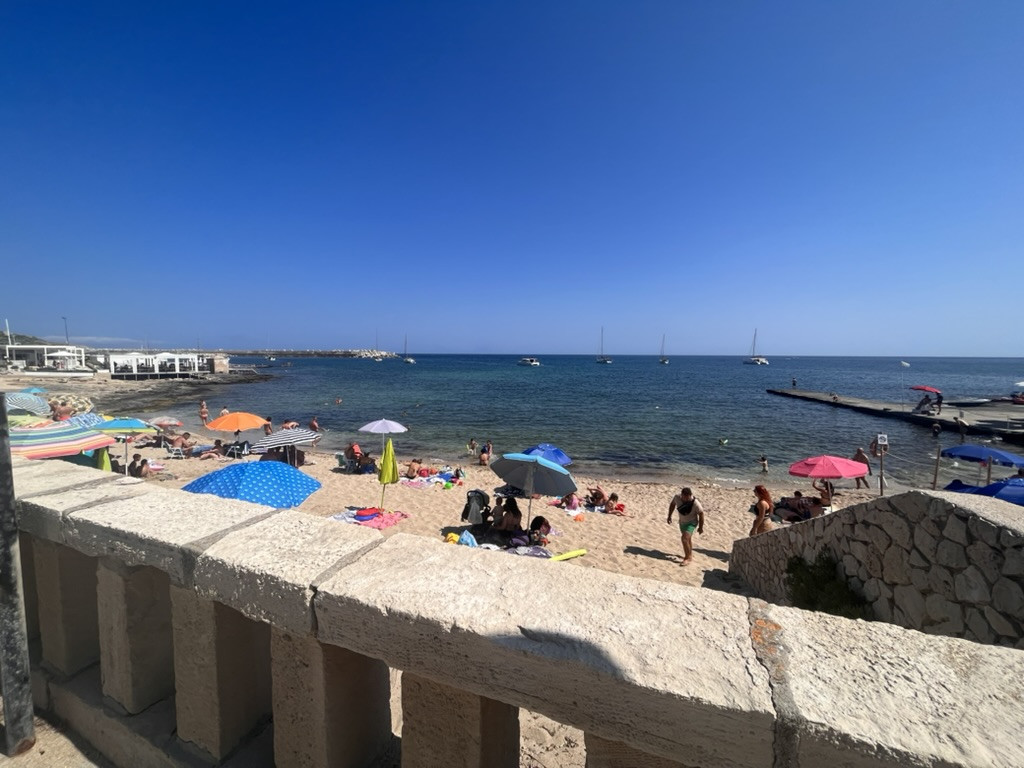 A small beach in Santa Maria di Leuca filled with swimmers and colourful umbrellas beside the calm blue sea.