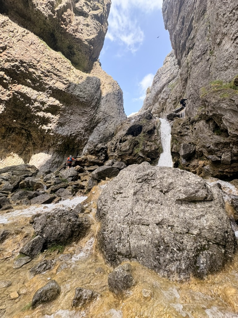 Hiker preparing to traverse a waterfall among the steep limestone cliffs near Malham Cove
