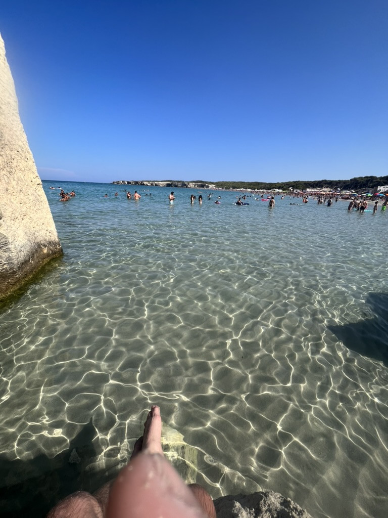 A view across the clear, shallow water at Torre dell’Orso, with swimmers and the beach beyond.