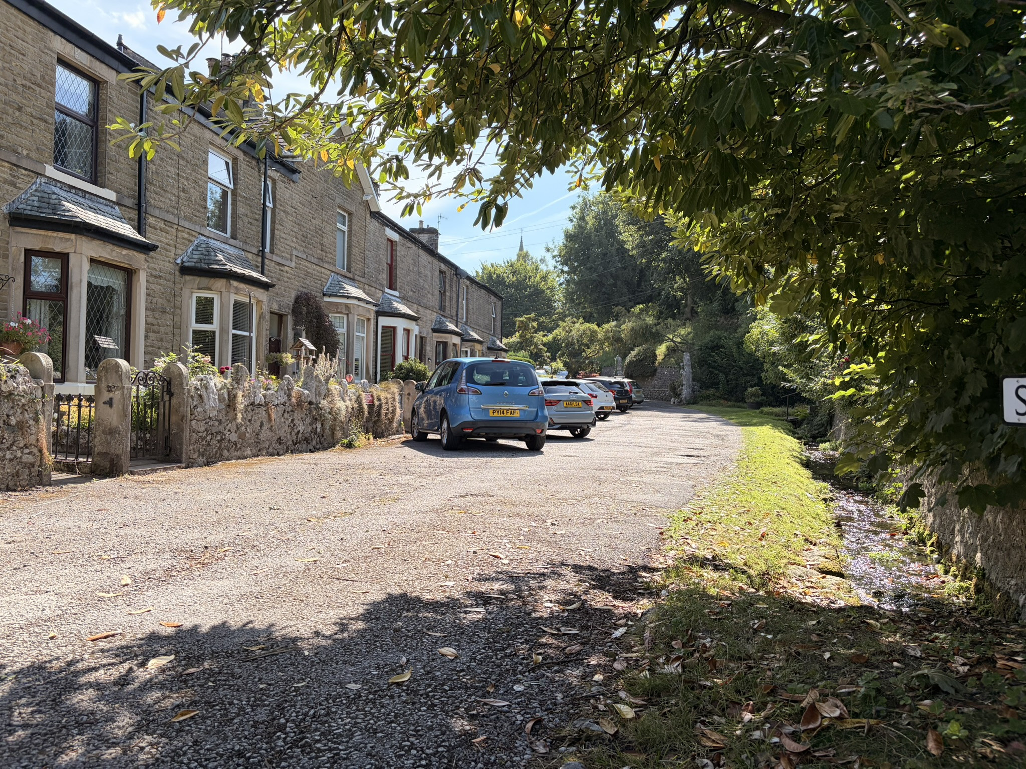 Picturesque village lane lined with stone cottages and a small tree-shaded stream beside the road