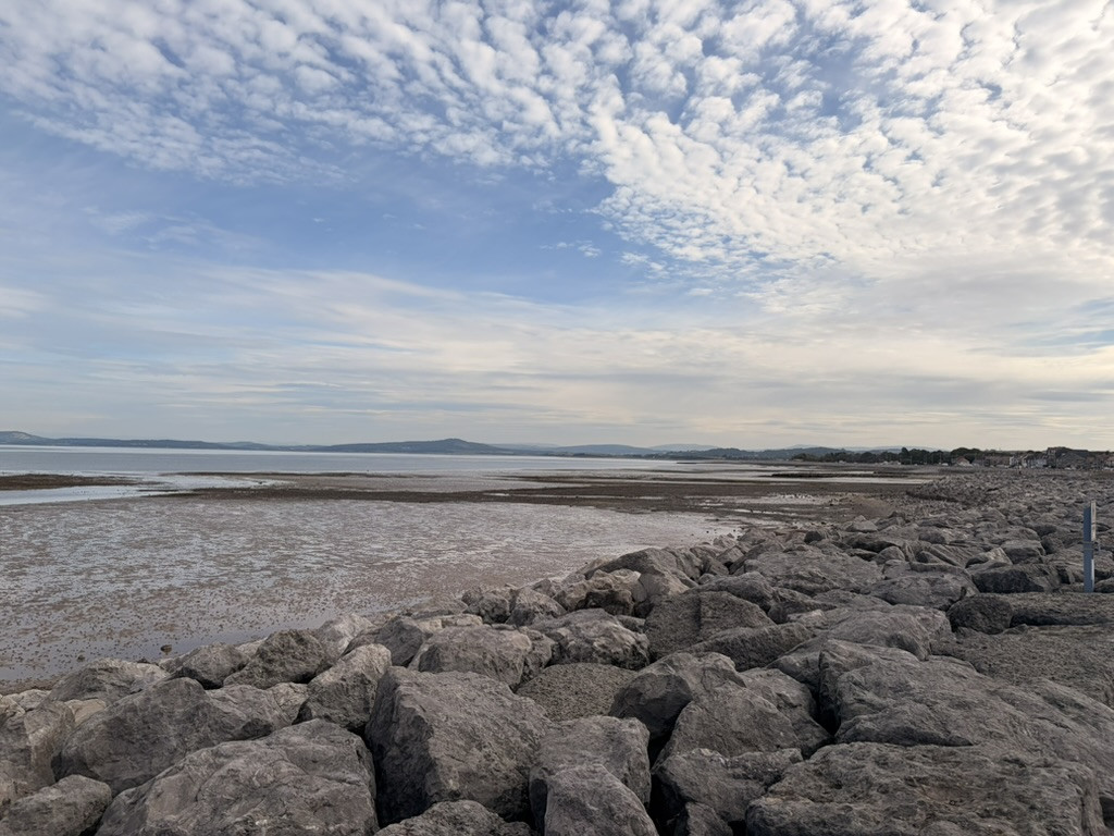 Rocky shoreline and wide tidal flats at Morecambe Bay beneath a textured cloud-filled sky