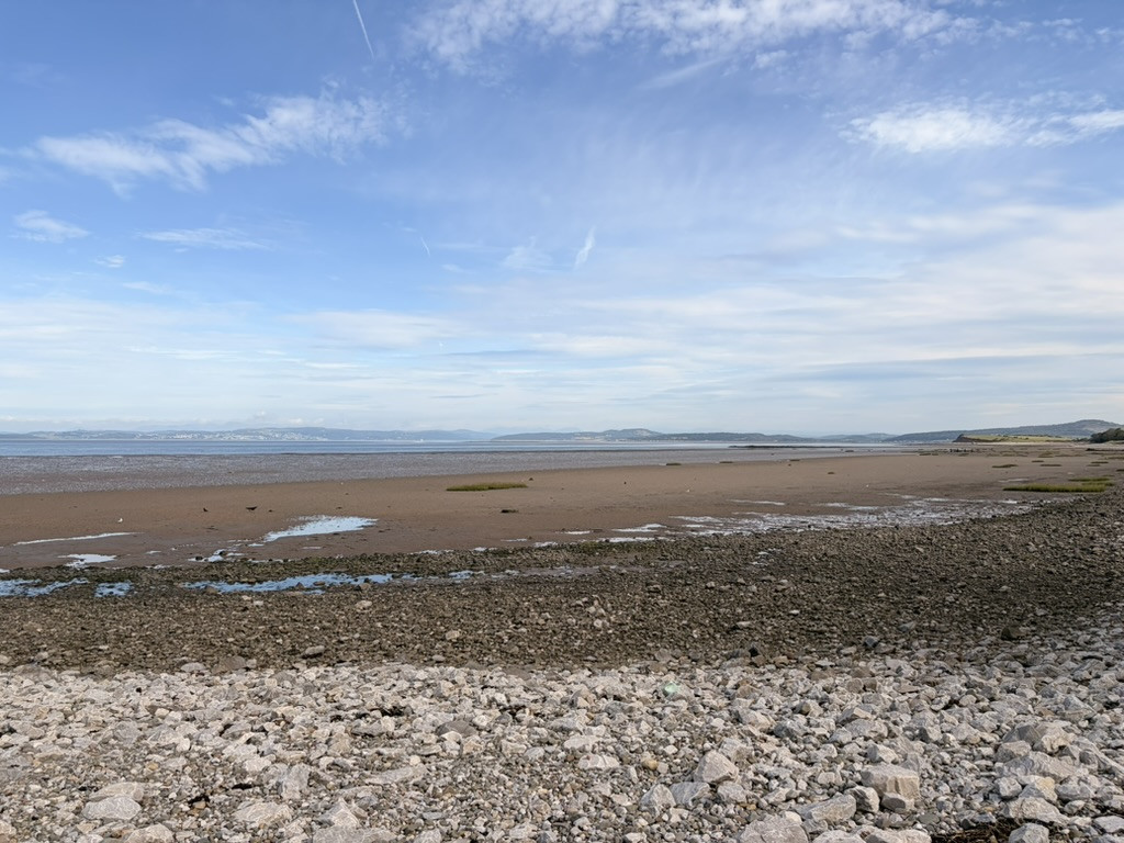 Expansive low-tide beach and stony foreshore looking across Morecambe Bay under a bright blue sky