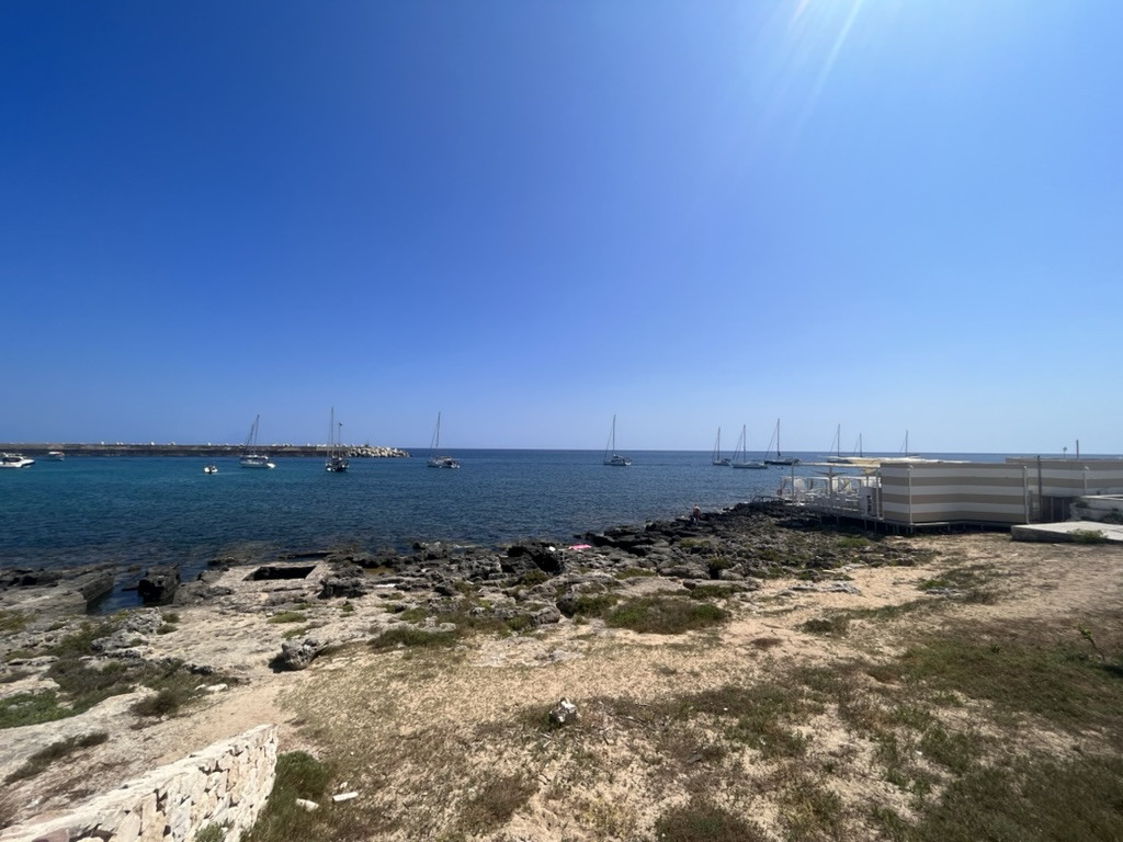 The rocky shoreline at Santa Maria di Leuca with sailing boats anchored on the clear blue sea.
