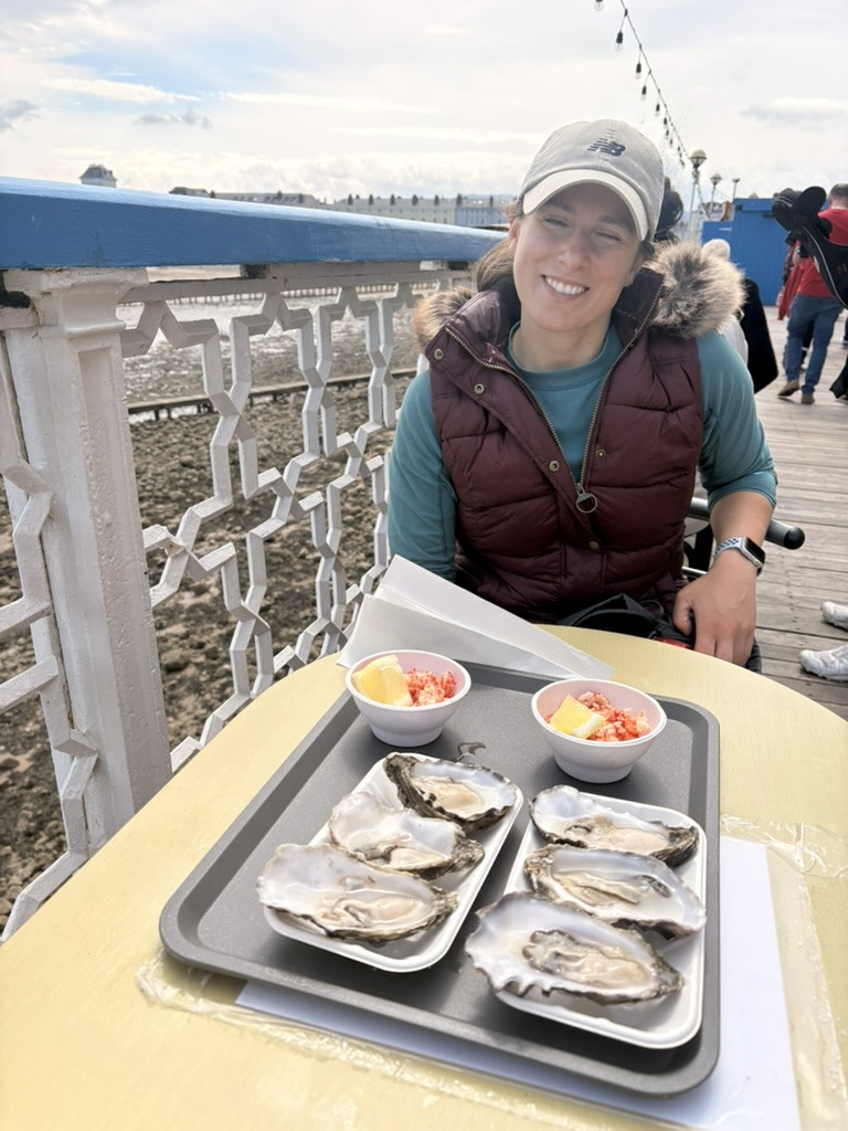 A smiling hiker sitting beside two trays of oysters on Llandudno Pier.