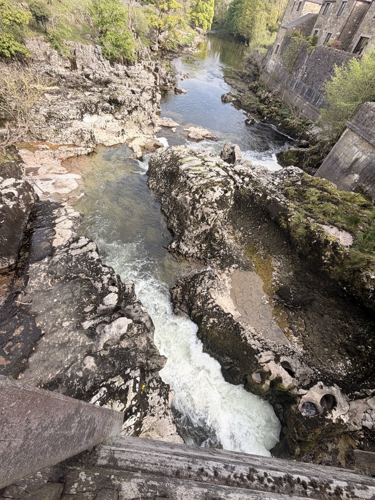 River Wharfe rushing through the rocky gorge at Linton Falls beside old stone buildings