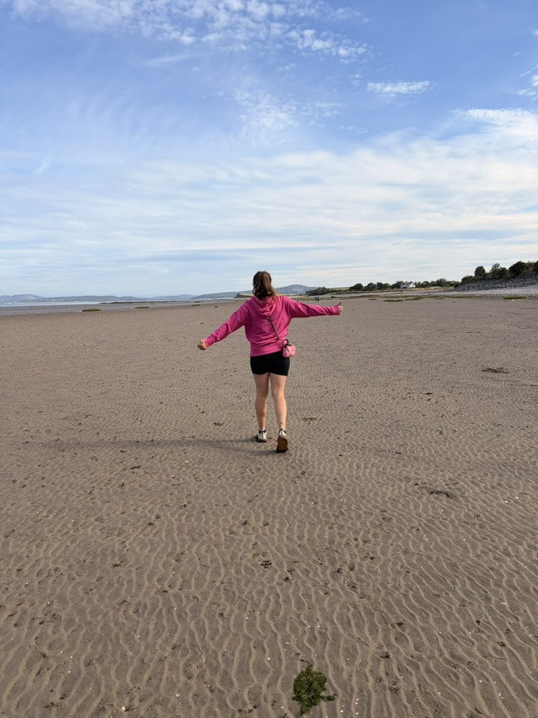 Walker stretching out her arms while crossing the broad sandy beach at low tide in Morecambe Bay