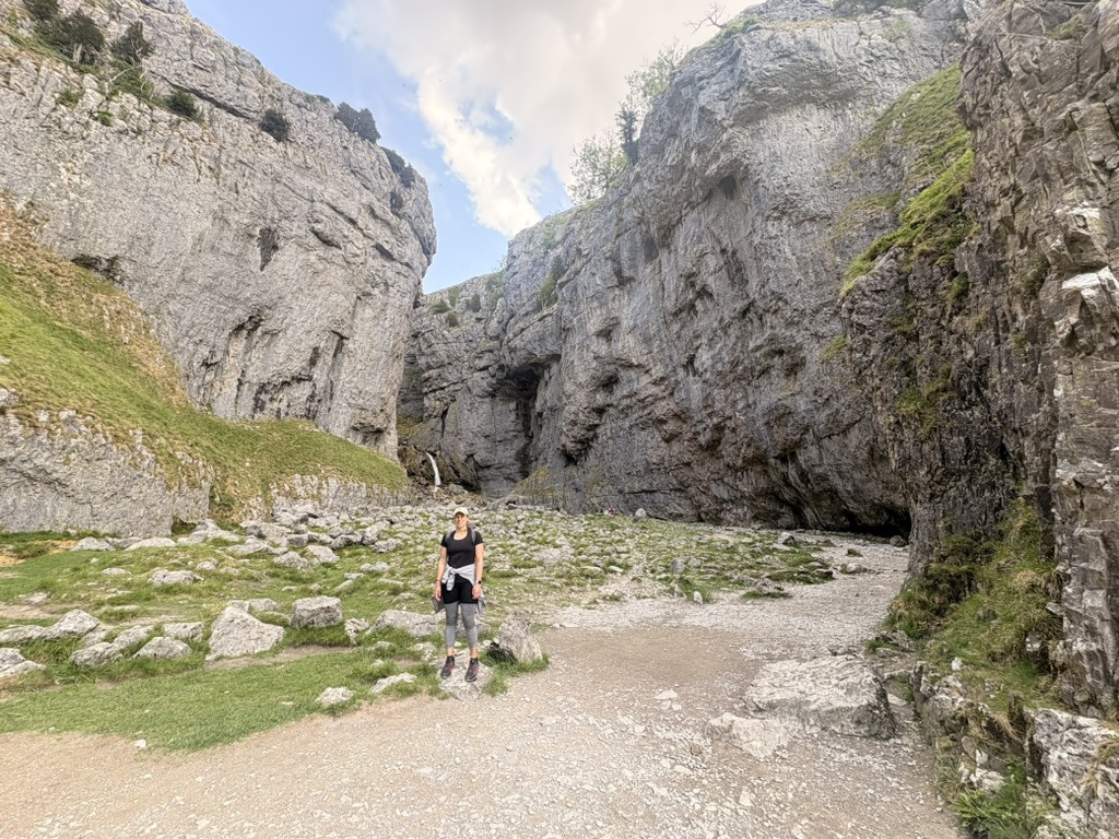 Walker standing beneath the towering limestone cliffs near Malham Cove on the Grassington to Malham route