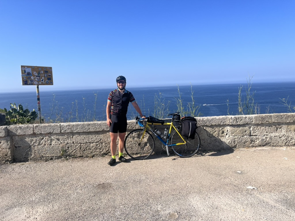 Ed standing beside his loaded touring bike at the start of the Adriatic Coast trip in Santa Maria di Leuca, with the sea behind him.
